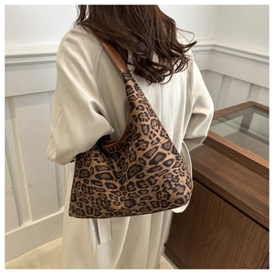 Detail of leopard print canvas tote bag with brown leather handles worn by a model