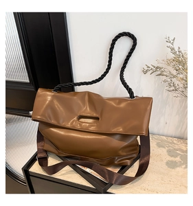 Close-up of brown leather tote with black woven handle and wide fabric shoulder strap