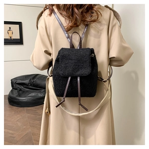 Detail of a mini black plush backpack with leather straps worn over a khaki trench coat