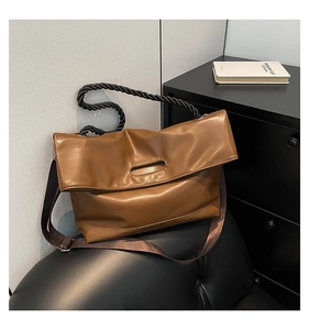 Close-up of brown leather tote bag with black braided rope handle on leather sofa