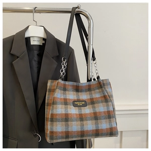 Detail of plaid tote bag with leather logo patch and metal chain strap on a blazer