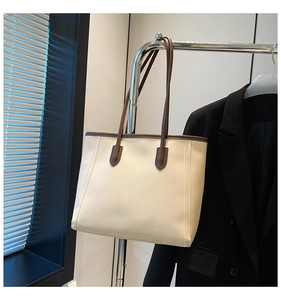 Detail view of large cream tote bag with contrast brown trim on a metal display rack