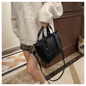 Detail of black pebbled leather bucket bag featuring white contrast stitching and gold rivets