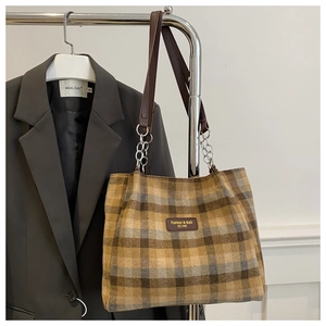 Detail of checkered tote bag featuring brown leather straps and silver metal chain links