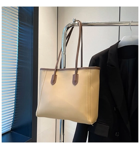 Close-up of minimalist apricot tote bag with brown contrast handles on a display rack