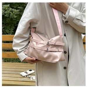 Close-up of pink glossy PU shoulder bag with dual leather buckle straps and silver hardware