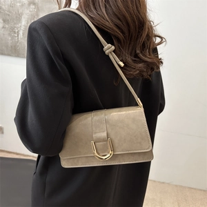 Minimalist beige leather shoulder bag with gold metal clasp on a model in a studio setting