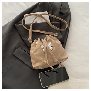 Detail of beige drawstring bucket bag with silver butterfly buckle and long shoulder strap