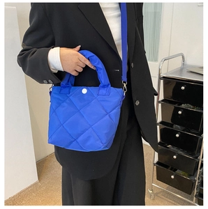 Close-up of royal blue quilted nylon bucket bag with white snap button and shoulder strap