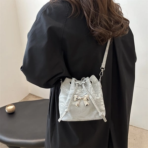 Light grey drawstring bucket bag with silver butterfly detail worn over a black coat