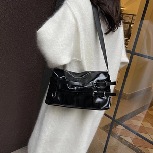 Glossy black PU leather shoulder bag with buckle straps shown on a model