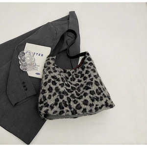 Detail of soft leopard print plush tote bag with black leather strap on a grey blazer
