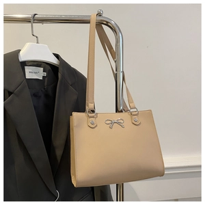 Detail of a beige faux leather tote bag featuring a silver metal butterfly ornament