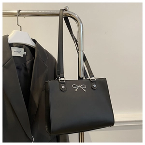 Detail of black matte leather tote bag featuring a silver metal butterfly ornament