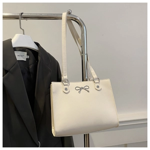 Detail view of cream tote bag with metal butterfly hardware and faux leather texture
