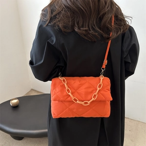 Sac à bandoulière matelassé orange vif avec grosse chaîne porté sur un manteau noir