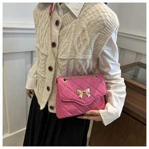 Detail of pink quilted crossbody bag with golden metal bow buckle worn by model
