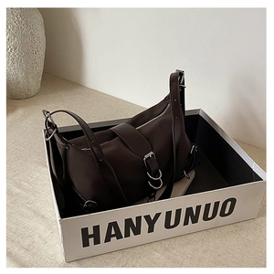 Detailed view of dark brown leather handbag with metallic buckle in branded packaging