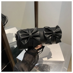 Detail of black cylindrical handbag featuring elegant leather bows and smooth zipper closure