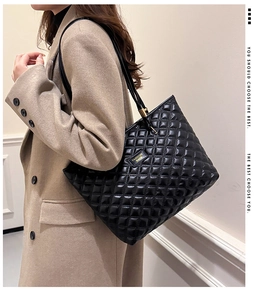 Detail of black quilted tote bag with golden metal logo on beige woolen coat background
