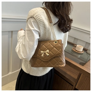 Brown quilted crossbody bag with gold bow clasp shown on model for size perspective