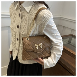 Close-up of quilted brown leather crossbody bag with golden bow clasp and chain strap