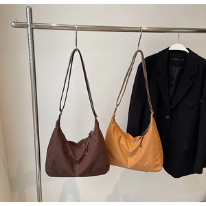 Détail des sacs fourre-tout en daim café et jaune gingembre suspendus devant un blazer noir