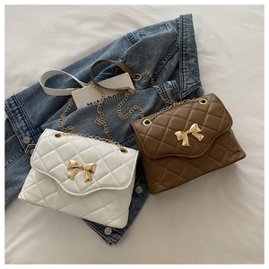 Detail of white and brown quilted crossbody bags with golden bow clasps and chain straps