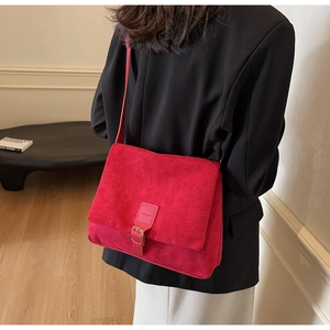 Detail of red suede tote bag with metal buckle and shoulder strap worn with dark suit