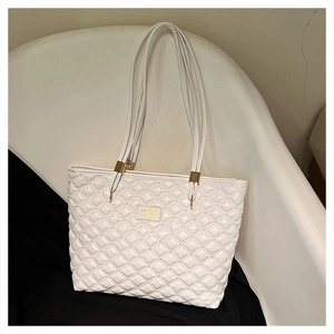 Detailed view of white quilted tote bag with diamond pattern and gold metal logo plate