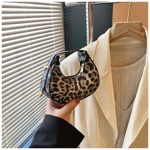 Detailed view of leopard print crescent bag held against stylish minimalist outfit