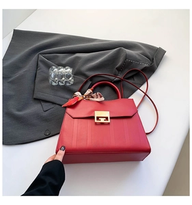 Detail of red textured leather handbag with gold metal clasp and floral silk scarf