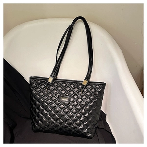 Detail of black quilted tote bag with gold logo plaque and elegant stitch pattern