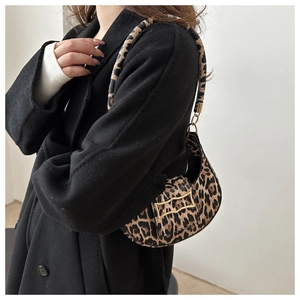 Detailed close-up of leopard print shoulder bag with gold metal buckle on black coat