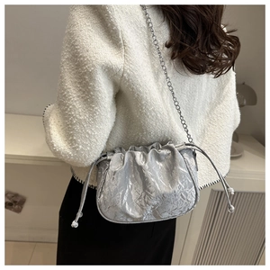 Silver pleated cloud bag with metallic chain strap worn by a model in a stylish setting