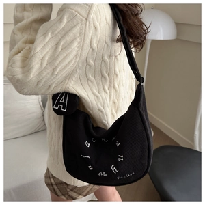 Detail of black corduroy hobo bag with white embroidery and adjustable shoulder strap
