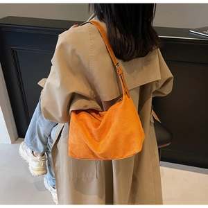 Detail view of vibrant orange suede tote bag worn with a stylish beige trench coat