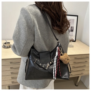 Detail of black leather shoulder bag featuring adjustable strap and plush bear charm