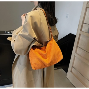 Detail view of a bright orange suede hobo shoulder bag styled with a beige trench coat