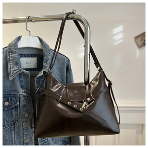 Detail of deep brown faux leather tote bag with metal buckles on denim jacket background