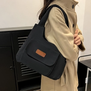 Sac fourre-tout minimaliste en nylon noir avec écusson en cuir marron sur l'épaule