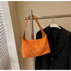 Detail view of bright orange suede underarm bag on a metal hanger with silver zipper