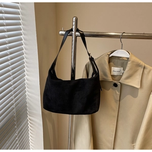 Close-up of minimalist black matte suede moon bag hanging on a metallic hanger with a coat