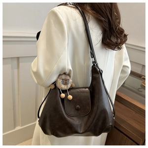 Borsa a spalla marrone scuro in PU con ciondolo di peluche indossata su abito bianco