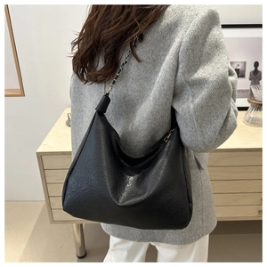 Détail du sac hobo en cuir noir texturé avec bandoulière en chaîne dorée sur mannequin