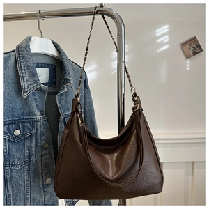 Détail d'un sac cabas marron texture lychee avec chaîne dorée sur une veste en jean