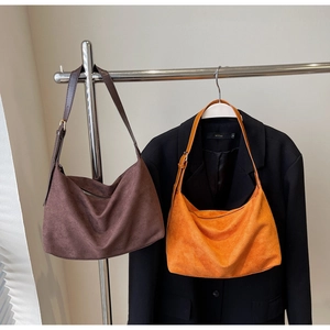 Close-up of matte suede hobo bags in dark brown and orange on a silver metal stand