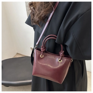 Detail of burgundy bucket bag featuring knotted handles and debossed FASHION text logo