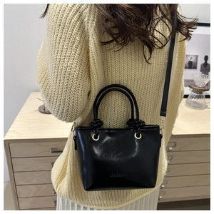 Detail of black glossy bucket bag with FASHION embossing and dual handles on model