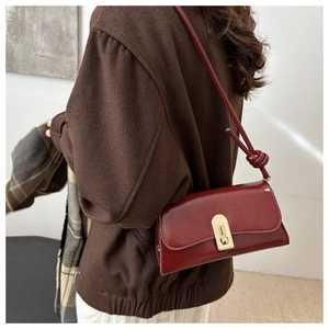 Detail of wine red glossy patent leather underarm bag with gold metal buckle and knot strap